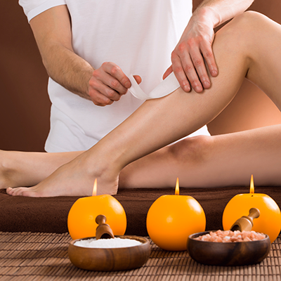 Professional beautician performing leg waxing for a female client